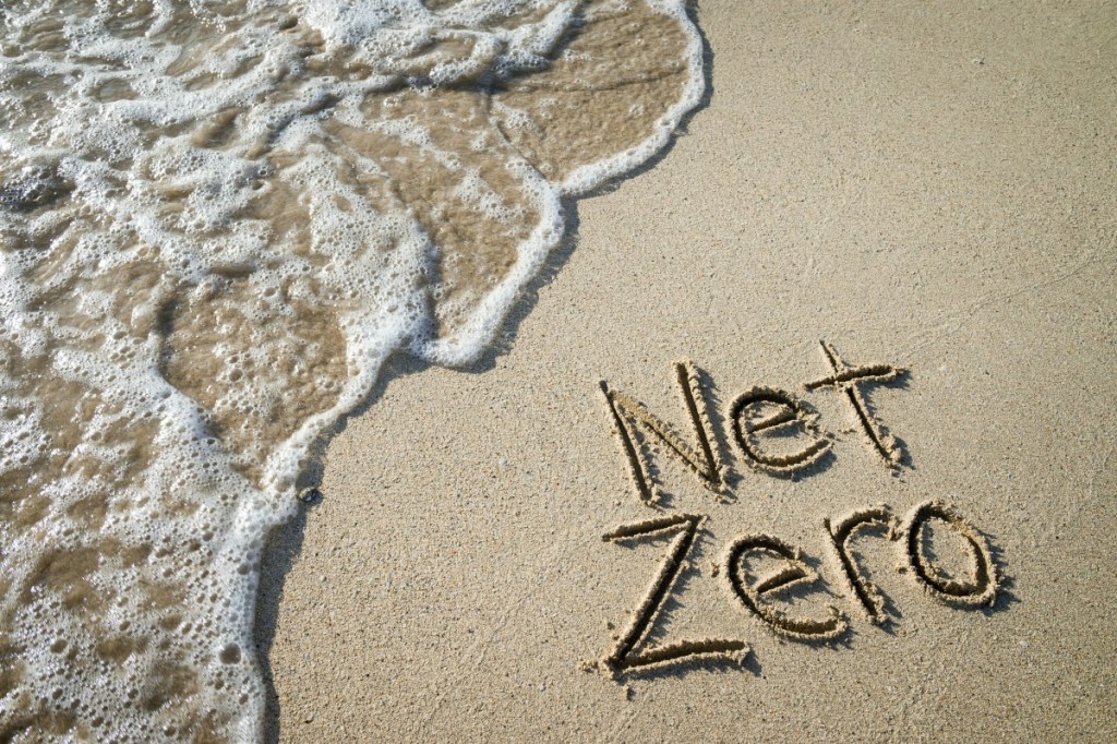 the picture shows a close up of the sea running up a beach with Net Zero written in the sand
